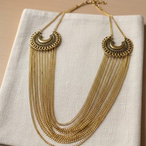 Antique gold layered statement necklace with dual crescent motifs and cascading chains on a beige background