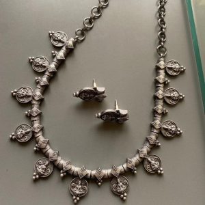 Oxidized silver coin necklace set with cylindrical beads on grey background