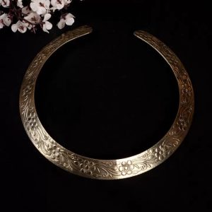 Antique gold tone rigid collar necklace with floral engraving on black background