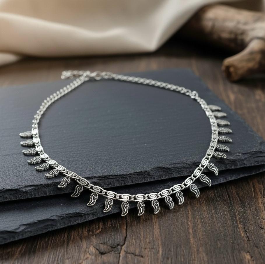Close up view of antique silver ethnic necklace featuring textured mango or leaf motifs on a link chain