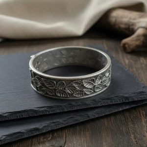 Wide antique silver hinged bangle with embossed leaf pattern on slate background