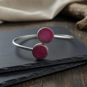 Silver bypass bangle bracelet with two round pink gemstones on slate background