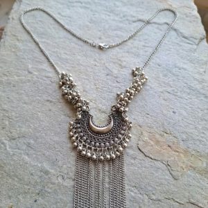 Antique silver bohemian necklace with crescent moon pendant, bead clusters, and long chain fringe laid on a stone surface