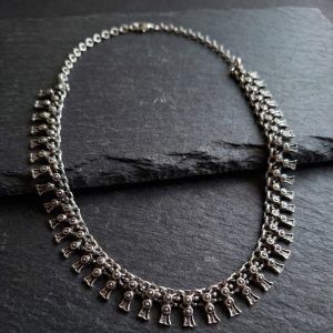 Oxidized silver tribal choker necklace with repeating tassel drop motifs resting on a dark slate stone surface