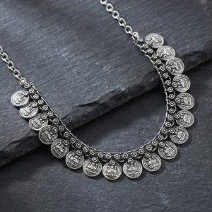 Oxidized silver traditional coin choker necklace arranged in a curve on a dark slate stone surface.