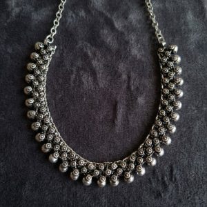 Oxidized silver tribal cluster choker necklace laid flat on a dark velvet background.