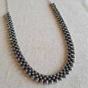 Oxidized silver tribal choker necklace with clustered metallic beads resting on a neutral linen surface.