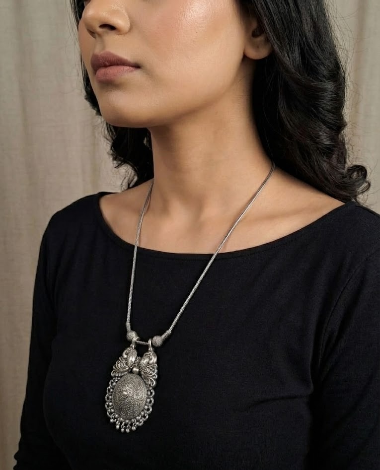 Front view of a woman wearing a long antique finish silver statement necklace over a black top, showing the ornate tribal pendant