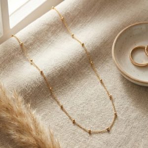Dainty gold chain with spaced gold beads on mannequin.