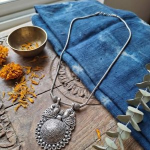 Studio shot of an oxidized silver tribal necklace with a large mandala and peacock design pendant displaying on a white jewelry bust