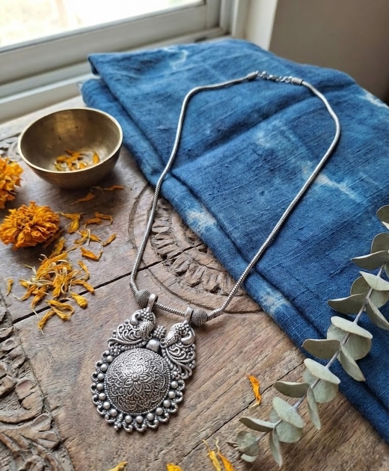Studio shot of an oxidized silver tribal necklace with a large mandala and peacock design pendant displaying on a white jewelry bust